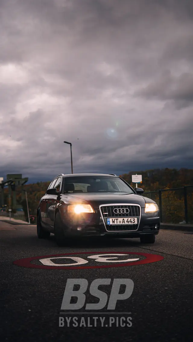 Audi A6 Avant mit Scheinwerferlicht auf einer Straße mit Tempo-30-Markierung unter Gewitterwolken