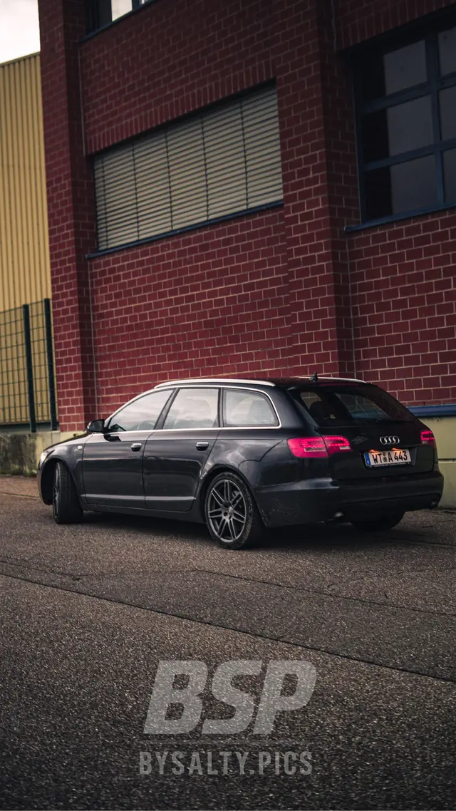 Audi A6 Avant in der Seitenansicht vor roter Backsteinwand mit leuchtenden Rückleuchten