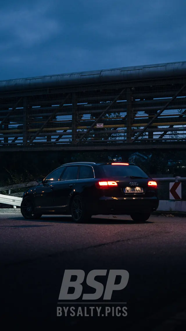 Audi A6 Avant mit Rücklichtern vor einer Industriebrücke in der Dämmerung