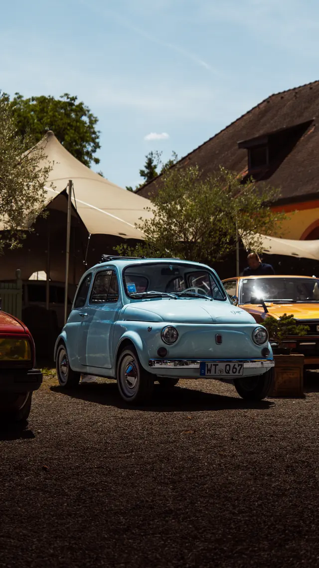 Hellblauer Fiat 500 Oldtimer unter Zeltdächern auf einem Fahrzeugtreffen