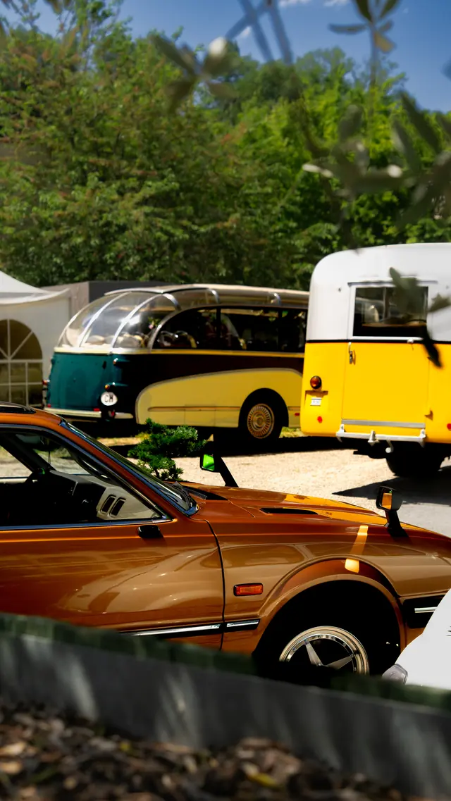 Orangefarbener Klassiker mit VW Bus im Hintergrund auf einem Treffen