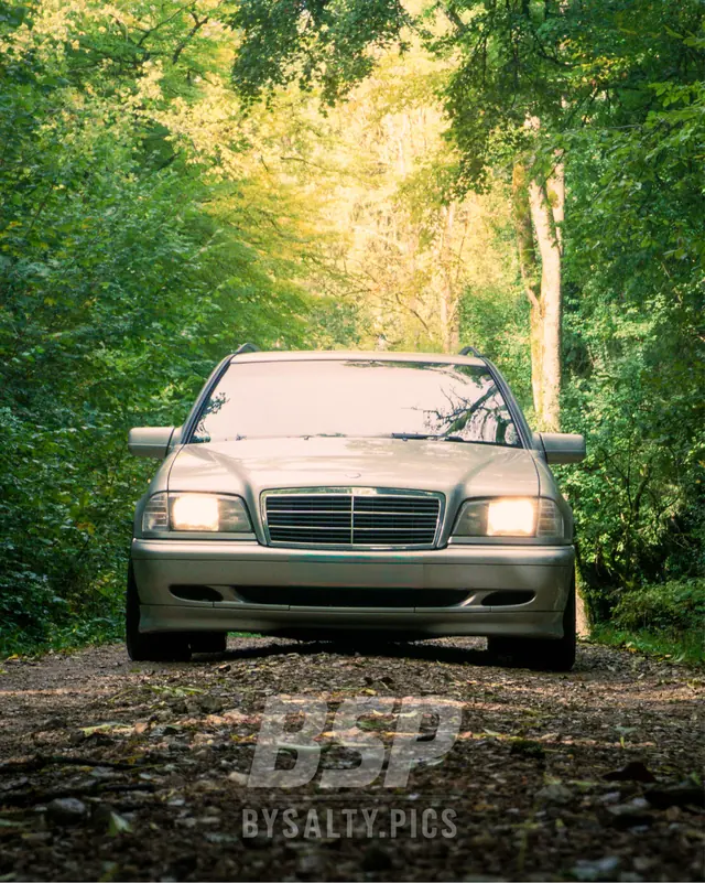 Mercedes-Benz C-Klasse in Silber mit eingeschaltetem Licht auf einem Waldweg